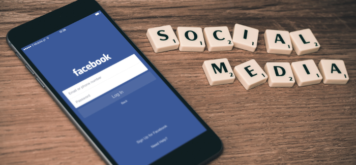 Smartphone mit geöffneter Facebook-App und Scrabble-Buchstaben SOCIAL MEDIA