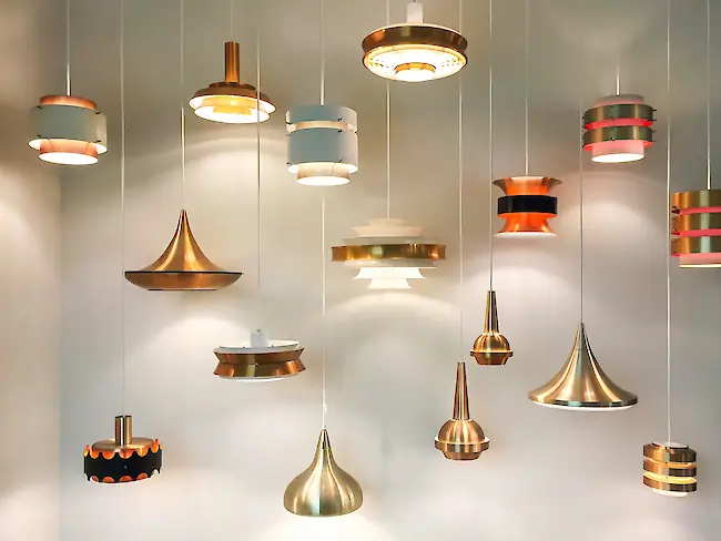 Eine Sammlung moderner Pendelleuchten in gebürstetem Messing und Weiß, in verschiedenen Höhen hängend vor einer neutralen Wand. Eine Sammlung moderner Pendelleuchten in gebürstetem Messing und Weiß, in verschiedenen Höhen hängend vor einer neutralen Wand.